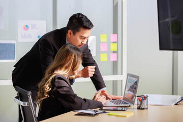 Millennial Asian successful professional male businessman mentor in formal suit coaching training helping female businesswoman secretary trainee working with laptop computer in office meeting room