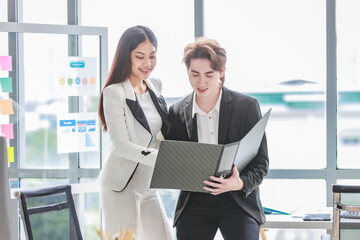 Millennial Asian successful professional female businesswoman mentor trainer in formal suit smiling helping explaining checking paperwork document in folder for male businessman trainee in office