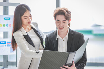 Millennial Asian successful professional female businesswoman mentor trainer in formal suit smiling helping explaining checking paperwork document in folder for male businessman trainee in office