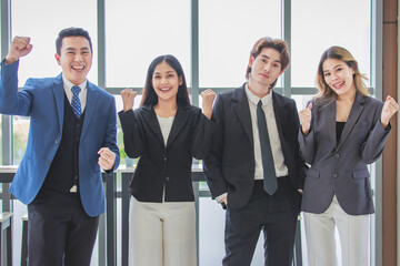 Millennial Asian successful professional male businessmen and female businesswomen colleagues standing side by side smiling laughing posing gesturing together in company office meeting room.