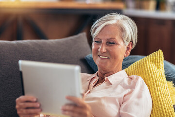 Mature woman using tablet computer while relaxing on sofa at home