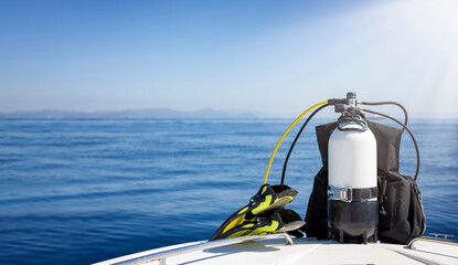 A scuba diving tank and gear standing on a boat bow with blue sea and sunshine as a banner with...