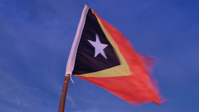 Flag of Timor Leste flying in strong wind against a blue sky from summit of Mount Ramelau, East Timor, Southeast Asia