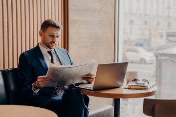 Male business company worker reading newspaper while working in cafe