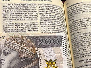 The Holy Bible in Polish, with a tab from a Polish banknote of 200 zlotys indicating a fragment from the Gospel according to St. Luke 16.13 "You cannot serve God and Mammon"