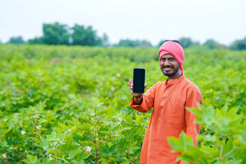 Indian farmer showing smartphone at cotton agriculture field.