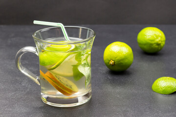 Lemon drink with green basil in a glass. Limes on the table.
