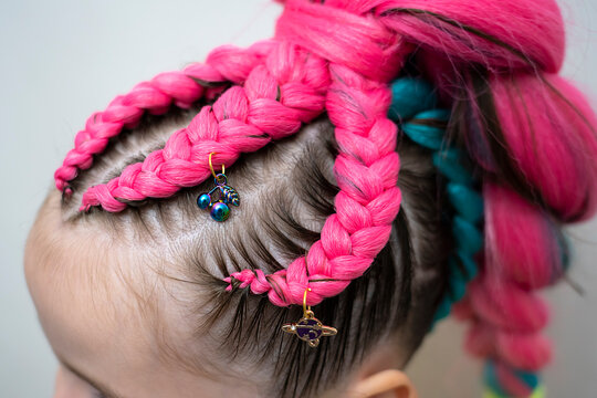 A fashionable hairstyle for a girl made of pink kanekalon braids with metal decorations (charms). High quality photo