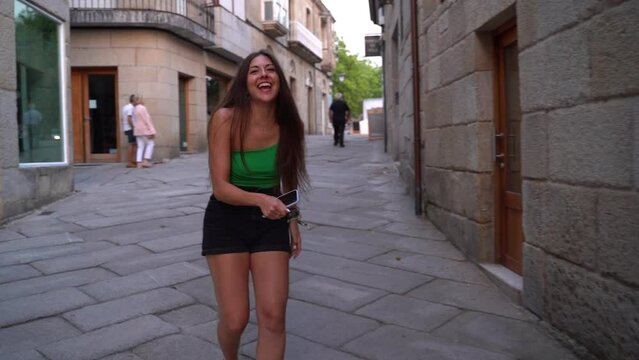 beautiful tourist girl walking forwards in the streets of Spain looking to camera laughing loud