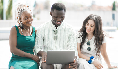 Gruppo ridente di giovani multietnici d'affari che lavorano su un laptop seduti insieme su una...