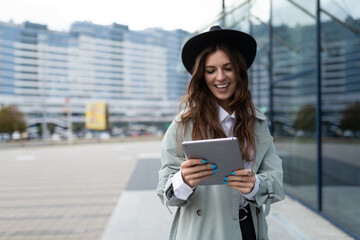 Fototapeta premium young stylish woman looking at a tablet against the backdrop of a glass facade of an office building in the city