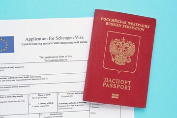Schengen visa application form in English and Russian language and passport on blue background. Prohibition and suspension of visas for tourists to travel to European Union and Baltic States concept