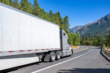 Bonnet gray big rig semi truck with reefer semi trailer transporting cargo climbing uphill on the winding mountain road