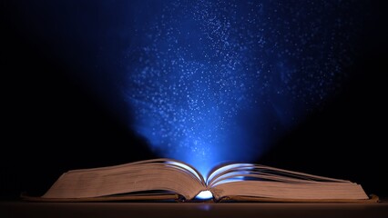 An open book illuminated by beam of blue light with smoke and dust particles on dark background. Textbook with open pages in rays of light. Book with fairytales, concept magical mysterious background.