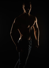 Fototapeta na wymiar Silhouette of topless guy posing in studio while standing and holding his posture