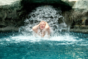Fototapeta na wymiar beautiful elder mature adult sexy redhead woman under the splashing water in the Spa Wellness pool enjoys the falling water