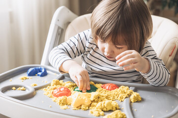Cute little boy playing with kinetic sand. Development of fine motor skills. Early sensory...