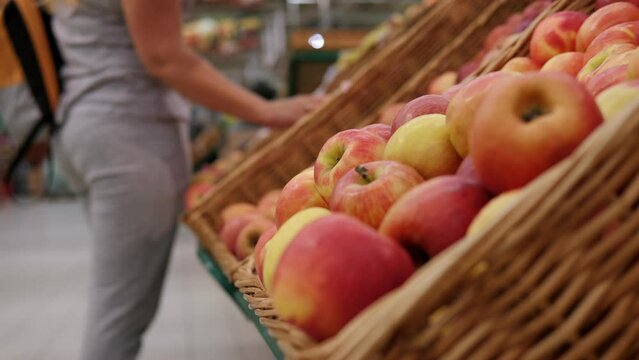 Close-up of boxes of ripe red apples in a large grocery store, with a blurry image of a woman picking apples in the background.