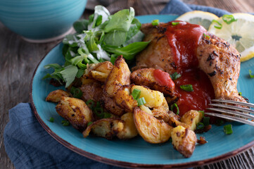 Fried potatoes on a plate with roasted chicken leg, spicy curry sauce and salad