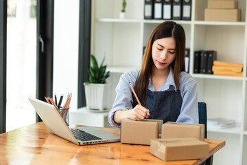  Asian woman hand using laptop, smartphone and tablet and writing notebook at office of her business online shopping. In home