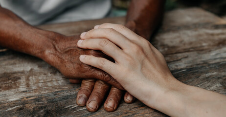 Hands of the old man and a woman hand on the wood table in sun light