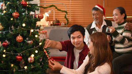 Loving young couple decorating Christmas tree, preparing for celebrating winter holidays together in cozy living room