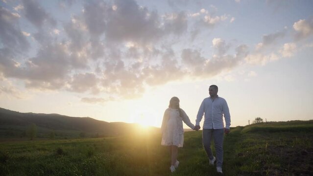 A guy and a girl in love are walking, hugging, resting in nature in the summer. Happy couple having fun on the background of the sunset in the field. Holding hands, looking at the bright sunrise.
