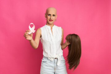 Woman suffering from cancer with a ribbon in her hand and holding a wig in the other hand