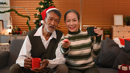 Joyful senior couple watching TV, spending leisure time in cozy winter weekend at home