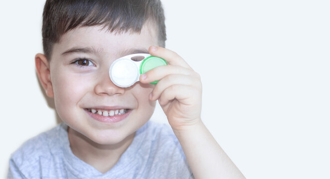 Cute Adorable Smiling Kid Holding In Front Of One Eye A Contact Lens Box Case,green And White Color.isolated On Background Child Wear Silicone Lenses For Better Vision,ophthalmology Concept,pro Con