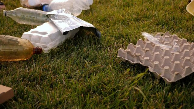 Close-up of volunteers collecting plastic garbage with tongs on the grass in the park. The concept of volunteering and environmental protection.