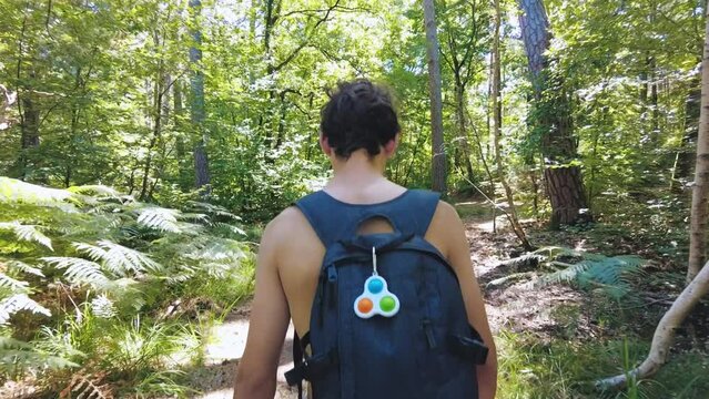 young shirtless teenage boy walking trough forest with backpack France sun flare