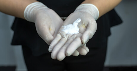 Close up cosmetologist hands wearing rubber gloves with white facial cream for facial mask in cosmetology spa clinic, Beauty Clinic Concept