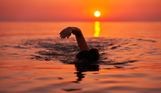 Young woman swimming in the sea on sunrise