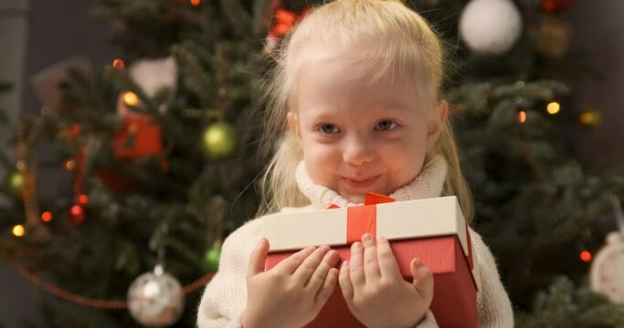 Smiling little girl got Xmas presents, happy and huggs him. Cute little blonde girl holds Christmas gift.