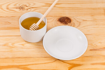 Honey in cup with wooden honey dipper and empty saucer
