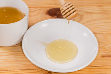 Honey flowing from the wooden honey dipper on to saucer