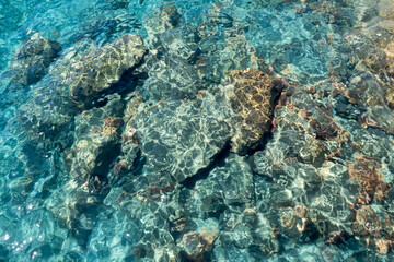 Rippled transparent aquamarine sea water surface with yellow rocks underwater