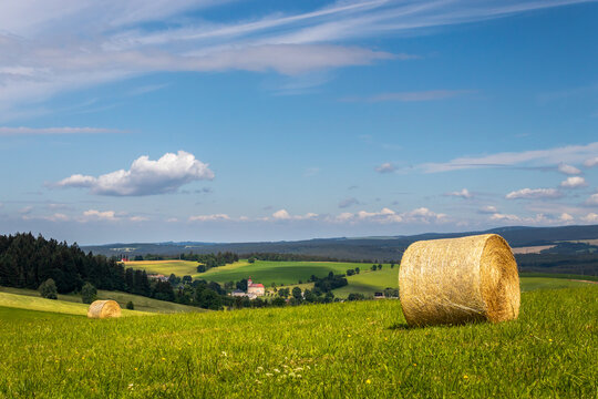summer landscape with a field with hay bale and blue sky with white clouds
