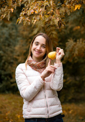 beautiful smiling girl in pink sort jacket holding yellow pear in her hands in autumn park