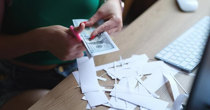 Woman counterfeiter cuts dollar bills with scissors at work table closeup
