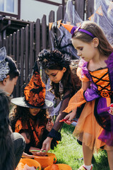 Multiethnic kids in costumes taking candies from buckets during halloween celebration outdoors