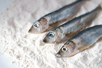 Three herrings on a plate with flour. Stages of cooking fish. Preparation for frying food.