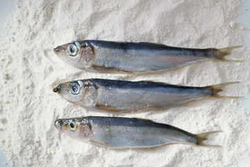 Three herrings on a plate with flour. Stages of cooking fish. Preparation for frying food.