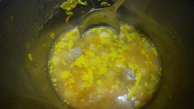 yellow soup with meatballs potatoes and vegetables in a gray pot and plate stirs with a spoon and ladle delicious food