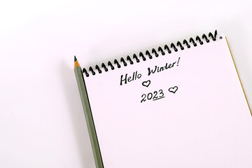Text hello winter. Handwritten note 2023. Hello winter black hand written lettering phrase. Text 2023.Design concept - Top view of spiral kraft notebook and ballpoint pen isolated on white background.