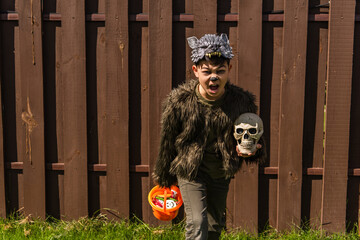 asian kid in werewolf costume holding skull and halloween bucket with sweets while showing angry...
