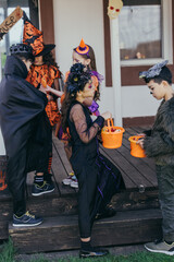 Multiethnic kids holding buckets with candies near friends in halloween costumes outdoors