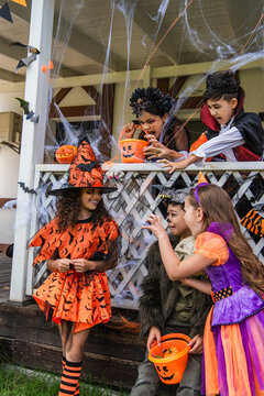 Multiethnic kids in halloween costumes grimacing near friend in witch hat outdoors