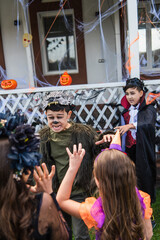 Asian boy in halloween costume grimacing near blurred friends in backyard